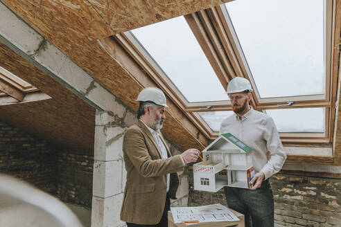 Architekten mit Helmen stehen mit einem Hausmodell auf einer Baustelle - YTF00412