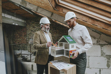 Architect showing house model to colleague at construction site - YTF00416