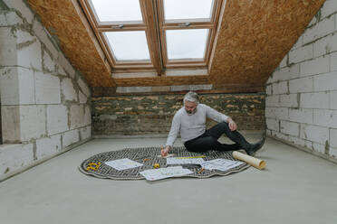 Architect working on project sitting on rug at construction site - YTF00422