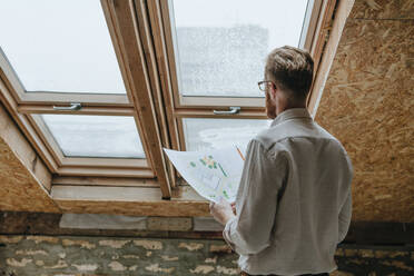 Architekt stehend mit Bauplan am Fenster auf der Baustelle - YTF00425