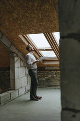 Architect with blueprint looking through window at construction site - YTF00429