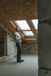 Architect standing with blue print near window at home - YTF00430