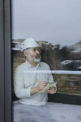Architect with diary making notes near window seen through glass - YTF00436