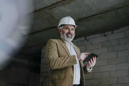 Glücklicher Geschäftsmann mit Schutzhelm und Tablet-PC auf einer Baustelle - YTF00444