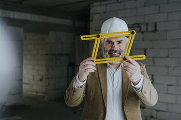 Smiling architect wearing hardhat looking through four-fold adjustable ruler - YTF00447