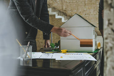 Architekt zeigt die Isolierung eines Modellhauses auf einem Schreibtisch auf der Baustelle - YTF00458