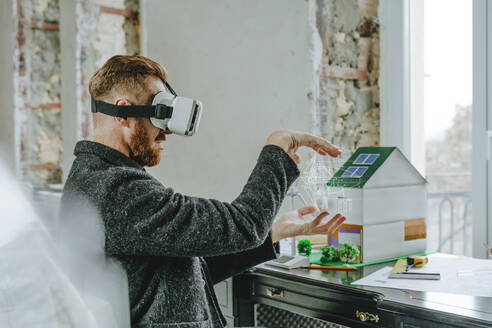 Geschäftsmann, der einen Virtual-Reality-Simulator trägt, gestikuliert auf einer Baustelle mit dem Entwurf einer Windkraftanlage - YTF00462