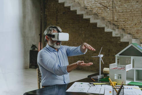 Geschäftsmann in VR-Simulator gestikuliert mit Modellhaus auf dem Schreibtisch - YTF00464