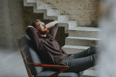 Happy businessman resting in chair at under construction site - YTF00475