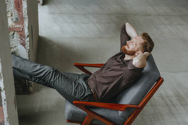 Geschäftsmann entspannt sich mit Händen hinter dem Kopf in einem Stuhl auf einer Baustelle - YTF00476