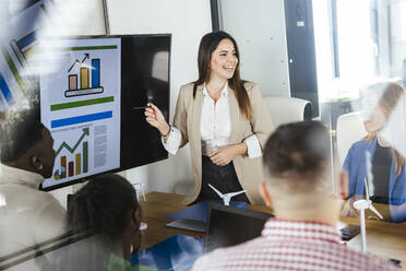 Happy businesswoman discussing renewable energies over graphs in meeting at office - LJF02402