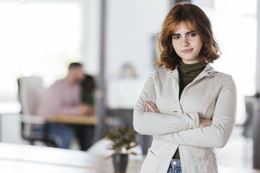 Confident businesswoman with arms crossed standing in office - LJF02407