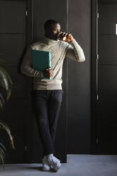 Businessman drinking coffee leaning on wall in coworking office - LJF02411