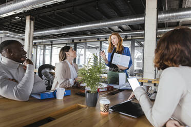 Rothaarige Geschäftsfrau, die mit Kollegen in einem Coworking-Büro über ein Dokument diskutiert - LJF02426