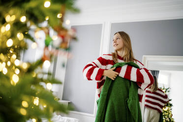 Lächelndes Mädchen mit grünem Pullover und Weihnachtsbaum im Vordergrund - MDOF00463