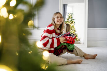 Girl with stack of sweaters sitting on carpet at home - MDOF00467