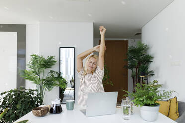 Freelancer stretching arms sitting at desk - TYF00576