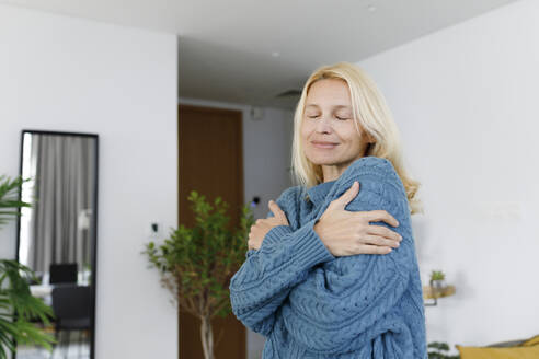 Smiling woman with eyes closed hugging self - TYF00587