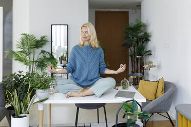 Smiling woman meditating on desk at home - TYF00595