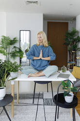 Smiling woman with hands clasped meditating on desk at home - TYF00596