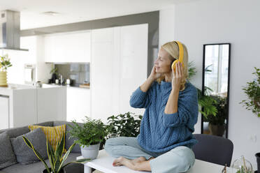 Woman wearing wireless headphones listening to music at home - TYF00597