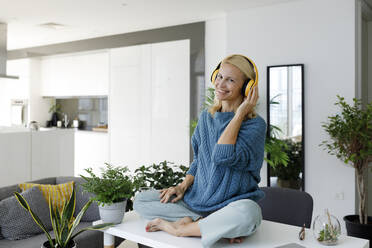 Happy woman wearing wireless headphones listening to music at home - TYF00598