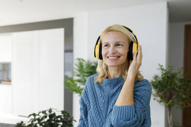 Glückliche Frau mit drahtlosen Kopfhörern beim Musikhören zu Hause - TYF00599