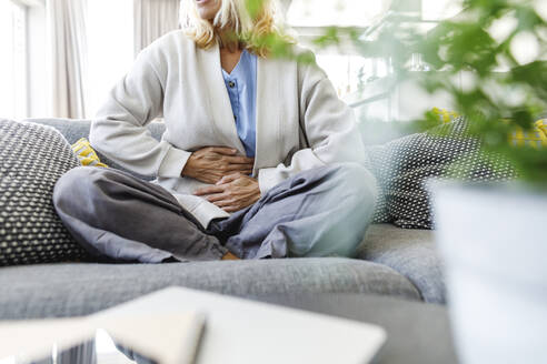 Woman having stomach ache sitting on sofa at home - TYF00612
