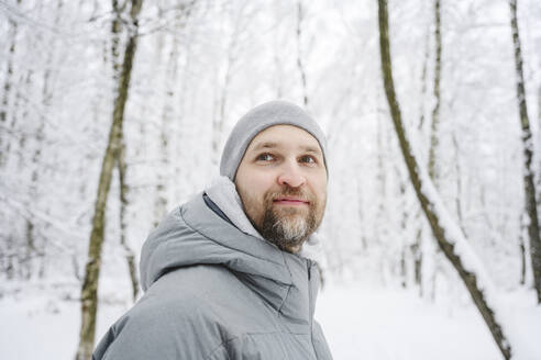 Smiling man wearing warm clothing at winter park - EYAF02498