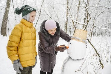 Junge baut Schneemann mit Großmutter im Park - EYAF02502