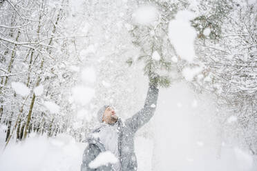 Mann schüttelt Schnee von einem Ast im Park ab - EYAF02505