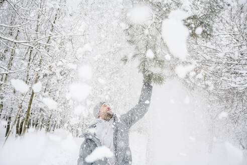 Mann schüttelt Schnee von einem Ast im Park ab - EYAF02505