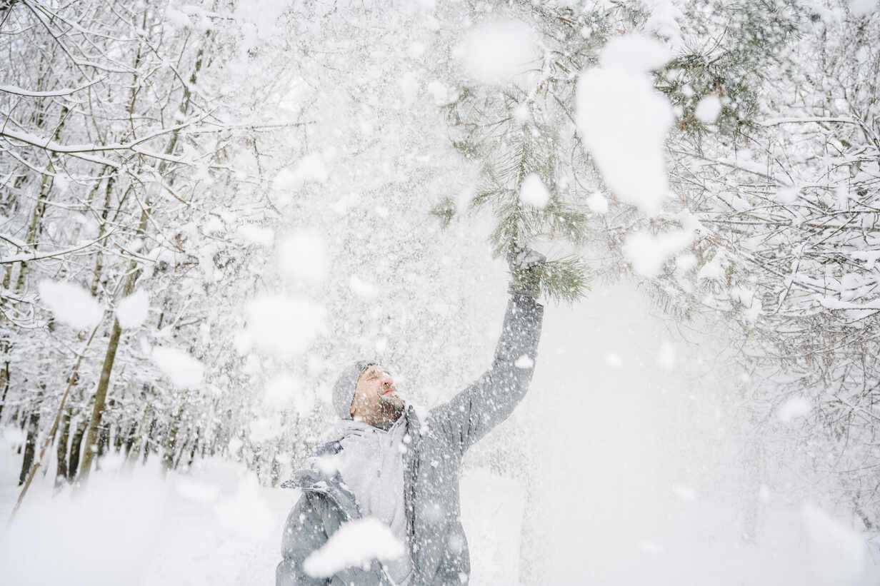 Mann schüttelt Schnee von einem Ast im Park ab, lizenzfreies Stockfoto