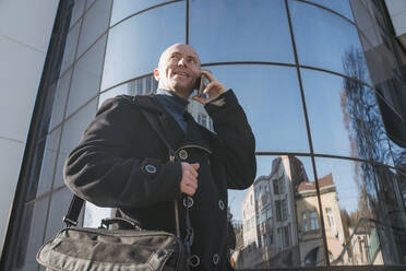 Älterer Geschäftsmann, der vor einem Gebäude mit einem Mobiltelefon spricht - OSF01282