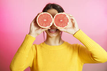 Smiling woman holding grapefruit halves against pink background - JSMF02620