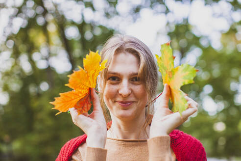 Lächelnde junge Frau mit Ahornblättern im Park - OSF01292