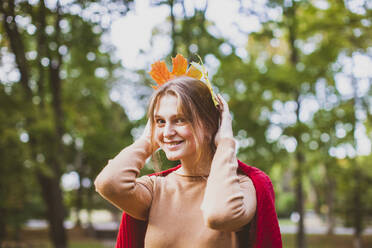 Lächelnde Frau mit Ahornblättern auf dem Kopf im Park - OSF01293