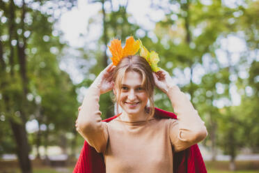 Lächelnde Frau spielt mit Ahornblättern im Park - OSF01294