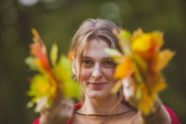 Blond young woman holding maple leaves - OSF01296