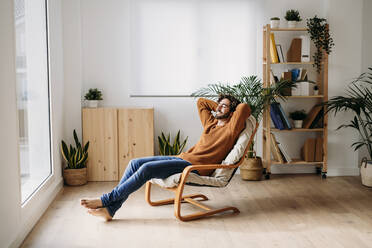 Happy man relaxing on armchair at home - EBBF07467