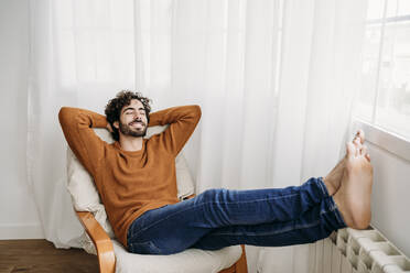 Happy young man with eyes closed relaxing in armchair - EBBF07524