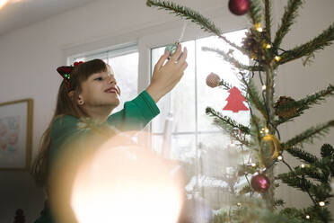 Smiling girl holding bauble hanging on Christmas tree at home - TYF00628