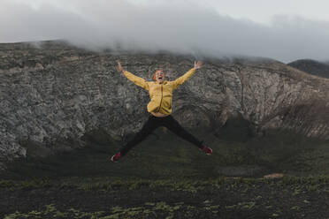 Carefree woman with arms outstretched jumping at Caldera Blanca volcano, Lanzarote, Canary Islands, Spain - DMGF00947