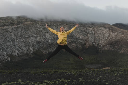 Unbekümmerte Frau mit ausgestreckten Armen beim Sprung auf den Vulkan Caldera Blanca, Lanzarote, Kanarische Inseln, Spanien - DMGF00947