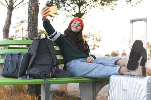 Happy girl taking selfie through smart phone sitting on bench - JAQF01106