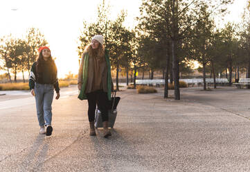 Mutter und Mädchen gehen mit Gepäck auf dem Fußweg bei Sonnenuntergang - JAQF01110