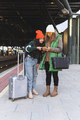 Daughter and mother searching in smart phone at railroad station platform - JAQF01119