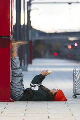 Mädchen liegt auf dem Rücken und benutzt ein Smartphone am Bahnsteig - JAQF01121