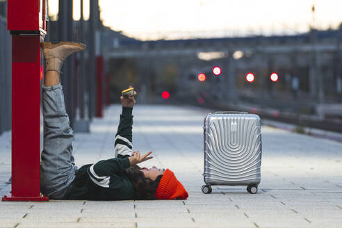 Mädchen spricht Selfie durch Smartphone liegend auf dem Bahnsteig - JAQF01122