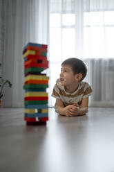 Junge auf dem Boden liegend mit einem Stapel Spielzeugblöcke zu Hause - ANAF00792